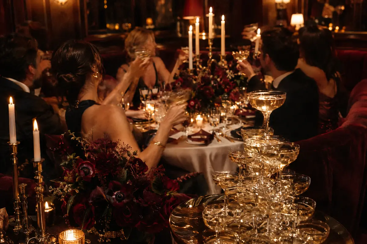 Guests toasting at a candlelit milestone birthday dinner beside a champagne tower
